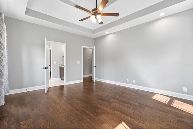 unfurnished bedroom featuring dark hardwood / wood-style floors, ceiling fan, and a tray ceiling