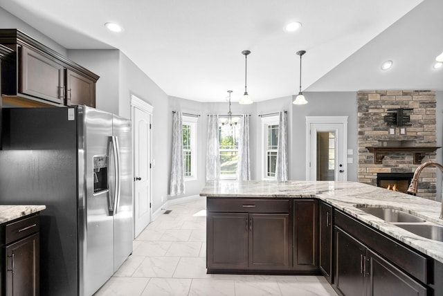 kitchen with light stone counters, sink, pendant lighting, stainless steel fridge with ice dispenser, and a stone fireplace