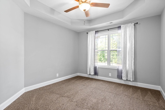 carpeted empty room featuring a raised ceiling, ceiling fan, and a healthy amount of sunlight