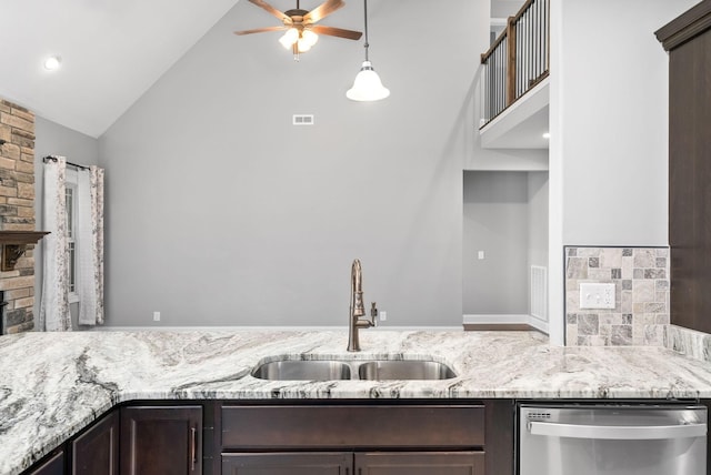 kitchen featuring dishwasher, sink, vaulted ceiling, light stone countertops, and dark brown cabinetry