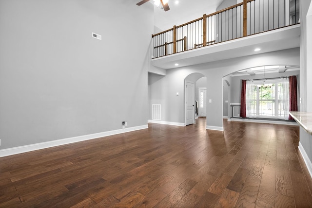 unfurnished living room with ceiling fan with notable chandelier, a towering ceiling, and dark hardwood / wood-style floors