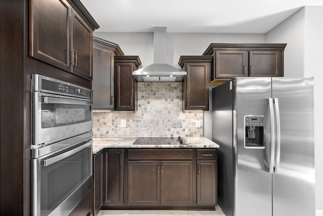 kitchen featuring backsplash, wall chimney range hood, light stone countertops, appliances with stainless steel finishes, and dark brown cabinetry