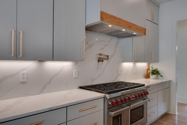 kitchen featuring double oven range, backsplash, gray cabinets, light stone counters, and custom range hood