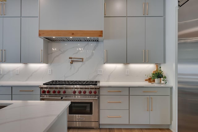 kitchen featuring decorative backsplash, gray cabinets, high end appliances, and light stone countertops