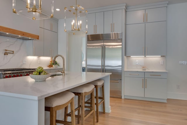 kitchen featuring decorative backsplash, light stone countertops, light wood-type flooring, stainless steel built in refrigerator, and decorative light fixtures