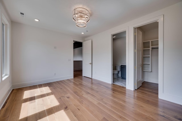 unfurnished bedroom featuring a spacious closet, a notable chandelier, ensuite bathroom, light hardwood / wood-style floors, and a closet