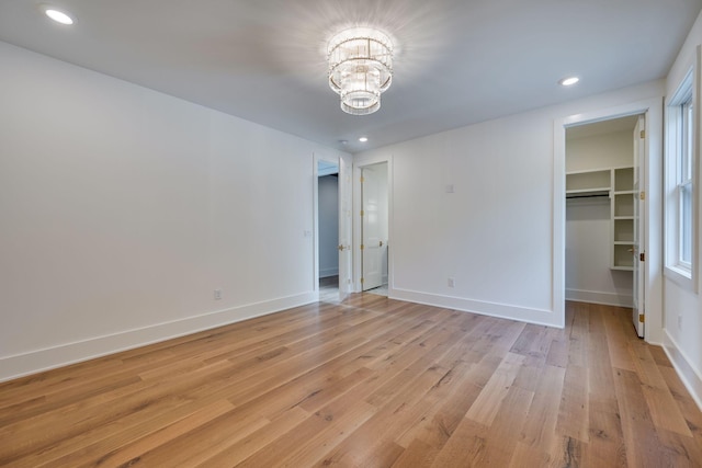 unfurnished bedroom with a chandelier, light hardwood / wood-style floors, a spacious closet, and a closet