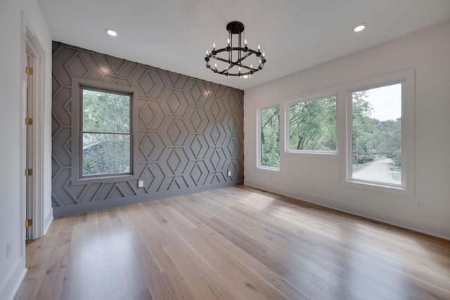 empty room featuring light wood-type flooring, plenty of natural light, and a notable chandelier