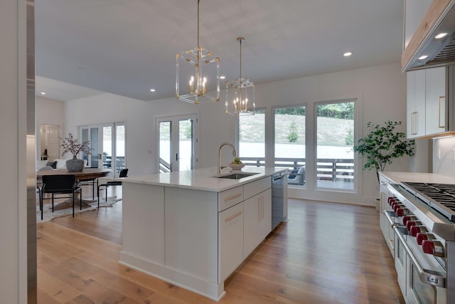 kitchen with white cabinetry, sink, stainless steel appliances, hanging light fixtures, and an island with sink