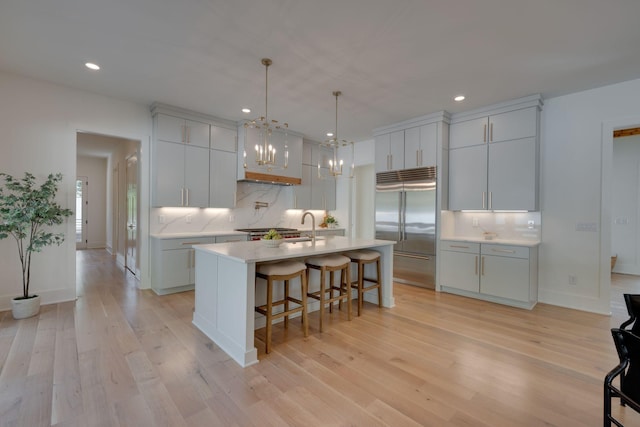 kitchen with tasteful backsplash, a breakfast bar, a large island with sink, pendant lighting, and built in refrigerator