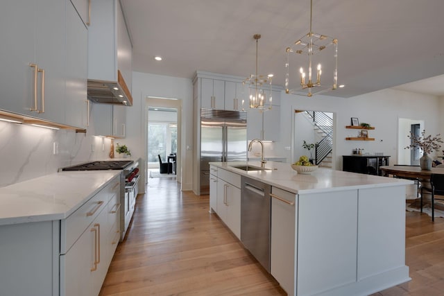 kitchen with decorative light fixtures, high end appliances, white cabinetry, and a kitchen island with sink