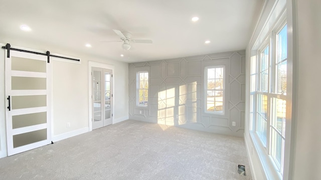 carpeted spare room with a barn door and ceiling fan