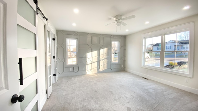 empty room featuring ceiling fan, a barn door, and light colored carpet