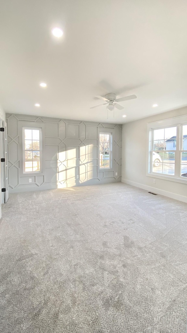 empty room featuring a wealth of natural light, ceiling fan, and carpet floors