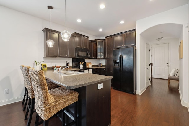 kitchen featuring a kitchen bar, kitchen peninsula, dark brown cabinets, black appliances, and hanging light fixtures