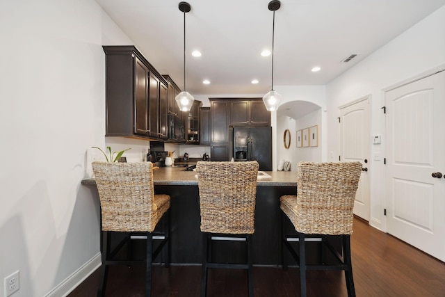 kitchen featuring a breakfast bar, dark brown cabinets, dark wood-type flooring, black appliances, and pendant lighting