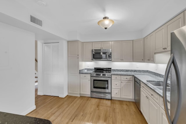 kitchen featuring appliances with stainless steel finishes, light wood-type flooring, and dark stone counters