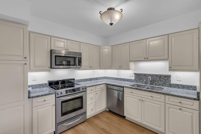 kitchen with appliances with stainless steel finishes, light hardwood / wood-style flooring, dark stone counters, and sink