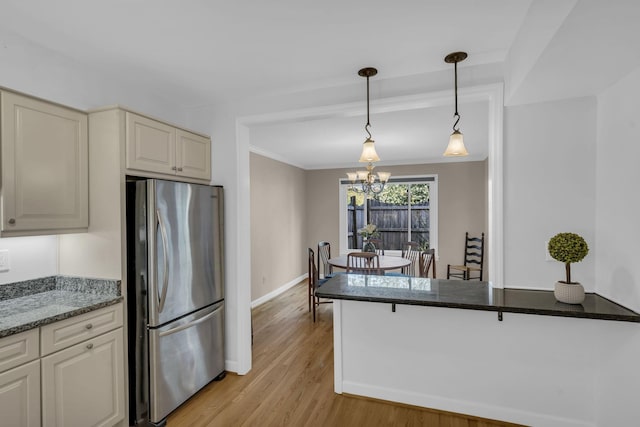 kitchen with stainless steel refrigerator, a notable chandelier, dark stone countertops, light hardwood / wood-style floors, and decorative light fixtures