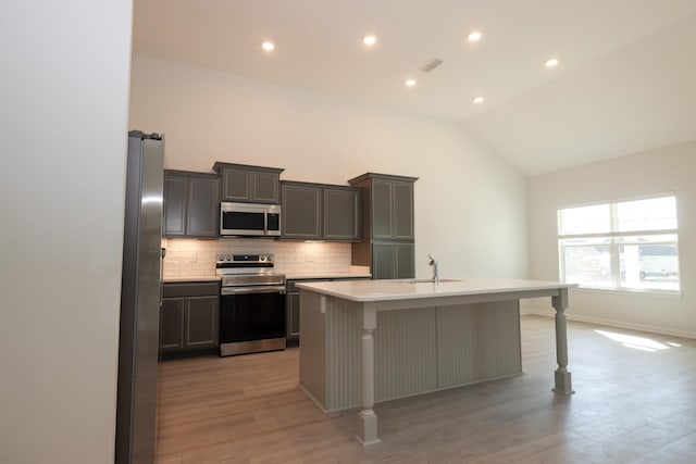 kitchen with a kitchen bar, tasteful backsplash, appliances with stainless steel finishes, a kitchen island with sink, and light hardwood / wood-style floors