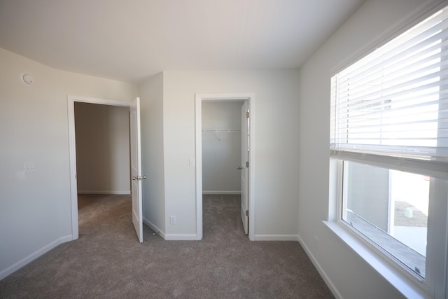 unfurnished bedroom featuring a spacious closet, a closet, and dark colored carpet