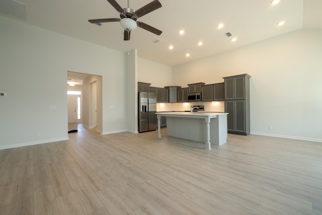 kitchen featuring high vaulted ceiling, a kitchen breakfast bar, a kitchen island with sink, stainless steel appliances, and light hardwood / wood-style flooring