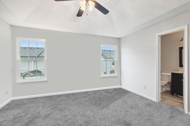 unfurnished bedroom featuring ceiling fan, a raised ceiling, connected bathroom, and multiple windows