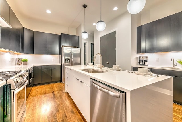 kitchen with stainless steel appliances, sink, an island with sink, and hanging light fixtures