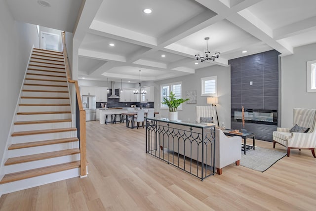 living room featuring coffered ceiling, an inviting chandelier, light hardwood / wood-style flooring, a large fireplace, and beam ceiling