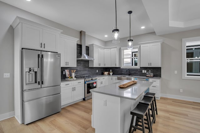 kitchen with wall chimney exhaust hood, a breakfast bar, high end appliances, white cabinets, and a center island