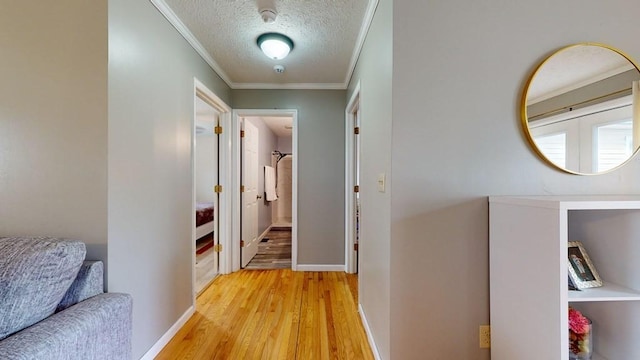 hallway with light wood-type flooring, a textured ceiling, and ornamental molding