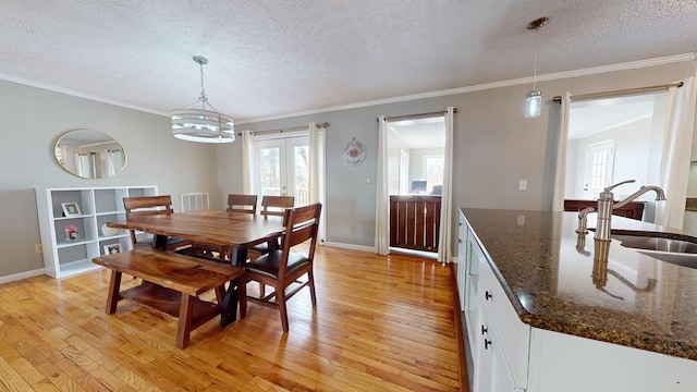 dining room with a textured ceiling, ornamental molding, sink, and light hardwood / wood-style flooring