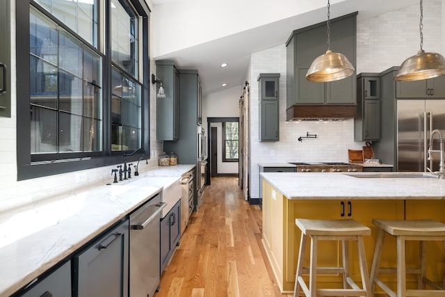 kitchen with appliances with stainless steel finishes, lofted ceiling, light stone counters, and pendant lighting