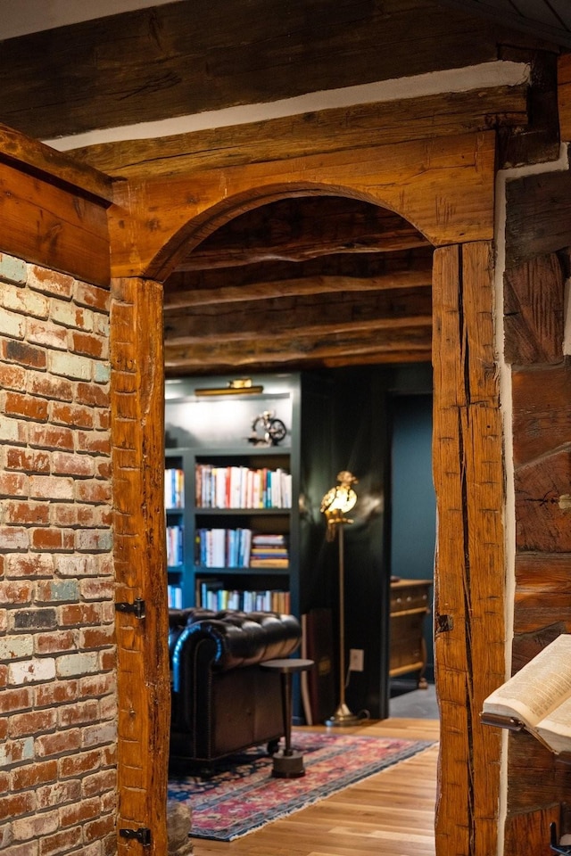 interior space featuring beam ceiling, wood-type flooring, and brick wall