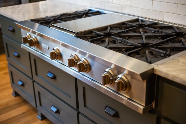 interior details with gray cabinetry, light hardwood / wood-style flooring, decorative backsplash, light stone countertops, and stainless steel range