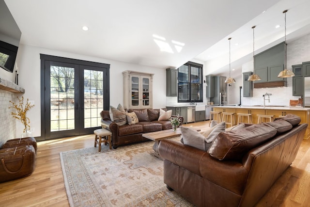 living room with sink, lofted ceiling, light hardwood / wood-style flooring, and french doors