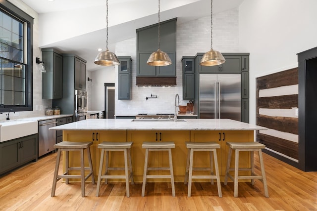 kitchen featuring a center island with sink, decorative backsplash, stainless steel appliances, and hanging light fixtures