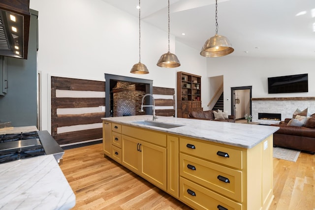 kitchen with lofted ceiling, a center island with sink, sink, hanging light fixtures, and a fireplace