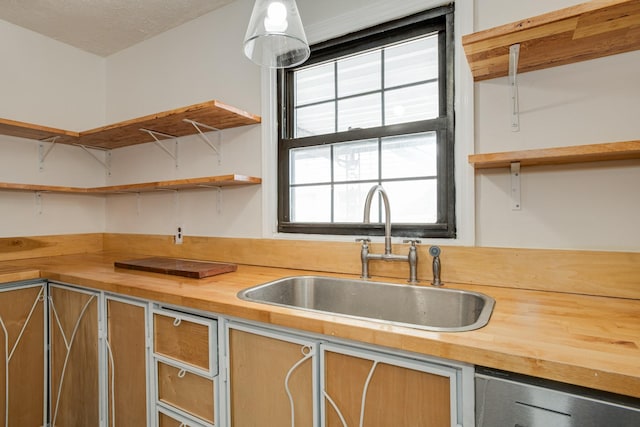 kitchen featuring sink, stainless steel dishwasher, a textured ceiling, and wood counters