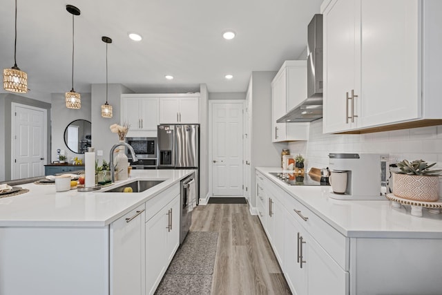 kitchen with stainless steel appliances, white cabinetry, hanging light fixtures, and wall chimney range hood