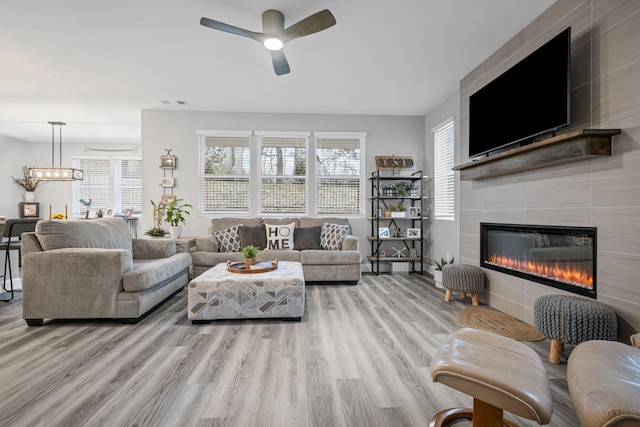 living room featuring a fireplace, light wood-type flooring, and ceiling fan