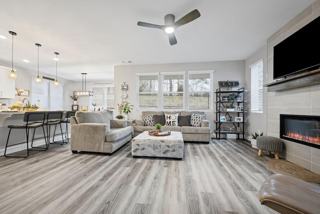 living room featuring a tile fireplace, ceiling fan, and light hardwood / wood-style flooring