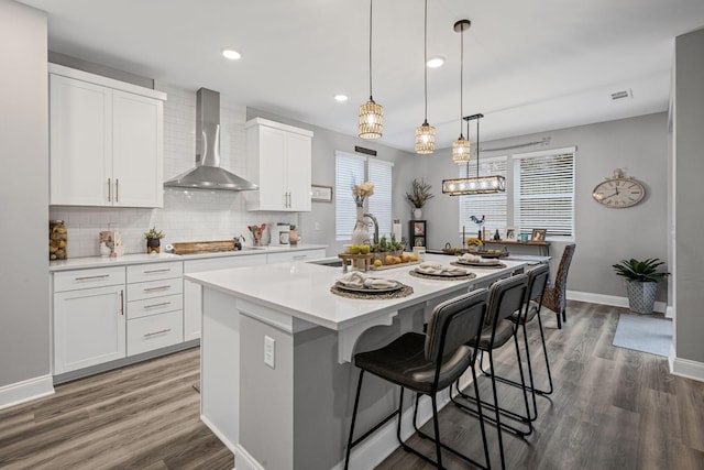 kitchen with wall chimney exhaust hood, a kitchen island with sink, sink, white cabinetry, and stainless steel gas stovetop