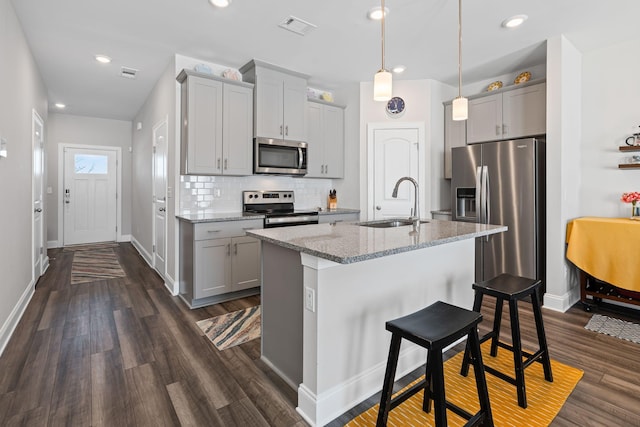 kitchen featuring light stone countertops, backsplash, stainless steel appliances, sink, and pendant lighting