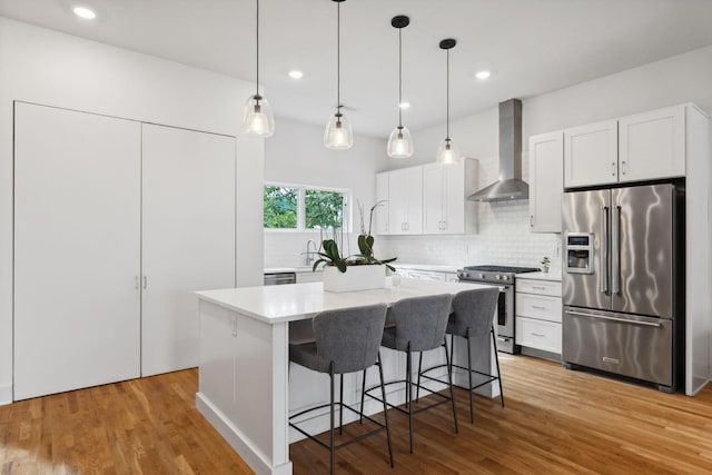 kitchen with a center island, wall chimney exhaust hood, decorative backsplash, white cabinets, and appliances with stainless steel finishes