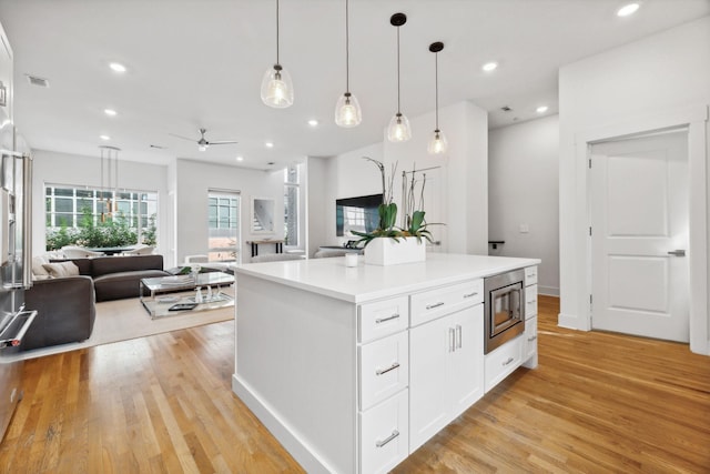 kitchen with a center island, stainless steel microwave, hanging light fixtures, ceiling fan, and white cabinetry