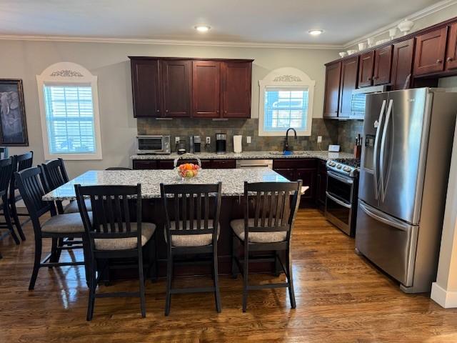 kitchen with a kitchen island, appliances with stainless steel finishes, dark wood-style flooring, a sink, and backsplash