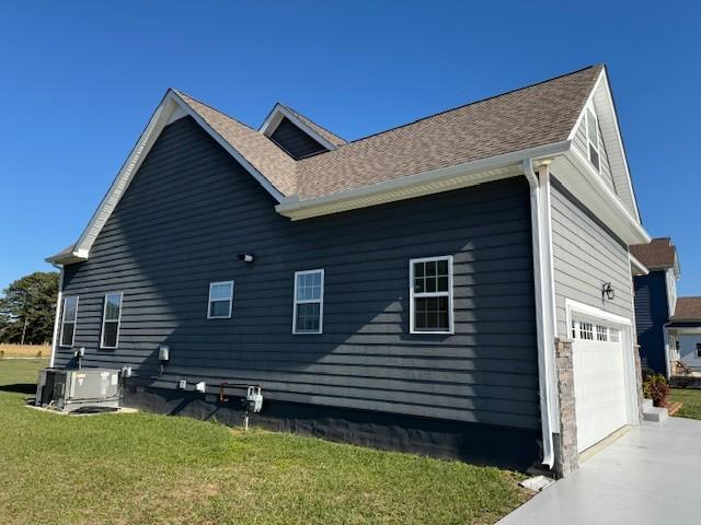 view of side of home with concrete driveway, roof with shingles, a yard, and central AC unit