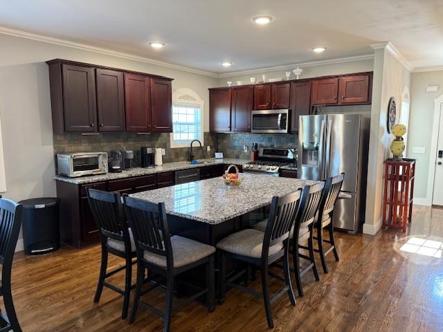 kitchen featuring a toaster, appliances with stainless steel finishes, dark wood finished floors, and a kitchen breakfast bar