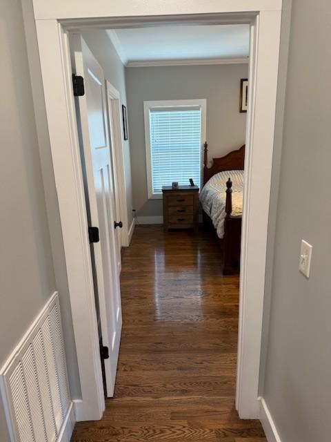 corridor with ornamental molding, dark wood-style flooring, visible vents, and baseboards